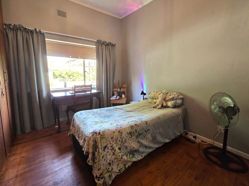 A bedroom featuring timber flooring and built-in cupboards, with natural light provided by a window fitted with security bars.