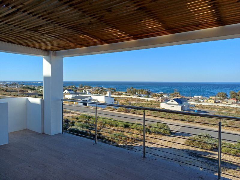 A spacious covered balcony featuring a timber slat ceiling, tiled flooring, and a stainless steel balustrade, offering expansive coastal and ocean views.