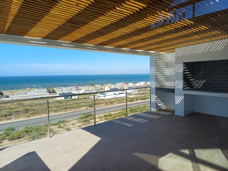 Spacious covered balcony featuring a built-in braai, modern tiled flooring, and stainless steel railing, offering expansive coastal and ocean views.