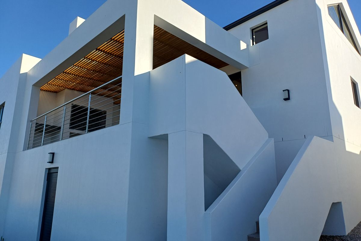 Modern exterior view of a multi-level home featuring clean white rendered walls, a timber-slatted balcony ceiling, and an external staircase.