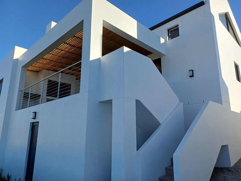 Modern exterior view of a multi-level home featuring clean white rendered walls, a timber-slatted balcony ceiling, and an external staircase.