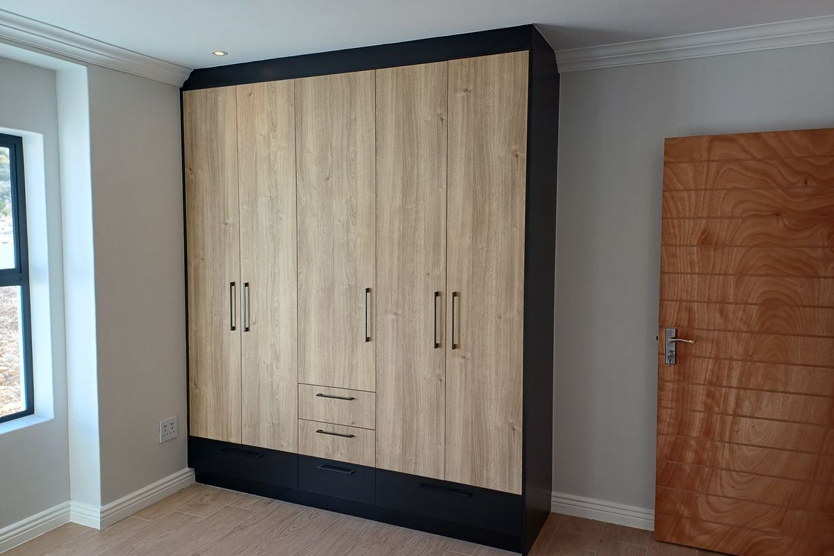 A modern bedroom featuring built-in floor-to-ceiling wardrobes with a wood-grain finish, black accents, and a contemporary horizontal-slat timber door.