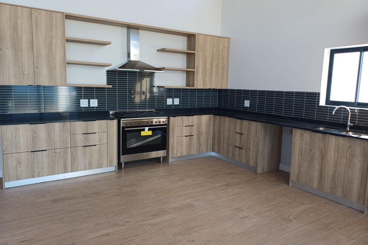 Modern kitchen featuring light wood-grain cabinetry, black stone countertops, a stainless steel gas stove with extractor fan, and dark subway tile backsplash.