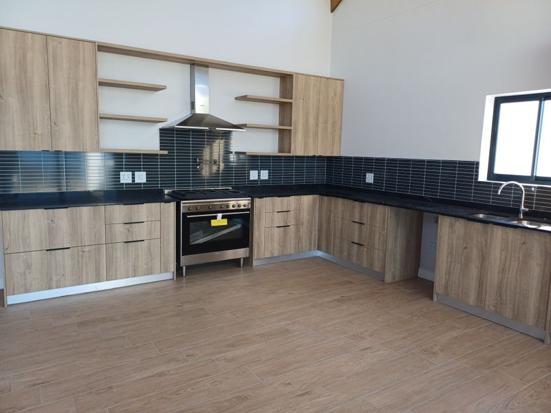 Modern kitchen featuring light wood-grain cabinetry, black stone countertops, a stainless steel gas stove with extractor fan, and dark subway tile backsplash.
