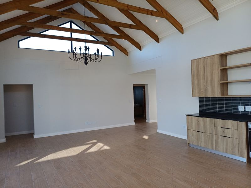 Spacious open-plan living area featuring high vaulted timber-beamed ceilings, modern wood-finish cabinetry, and sleek black tiled kitchen splashback.