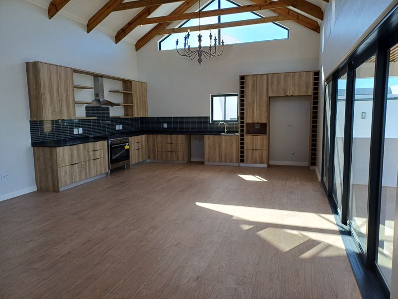 Spacious open-plan kitchen featuring modern wood-finish cabinetry, black tiled backsplash, built-in oven, and high vaulted ceilings with exposed timber trusses.
