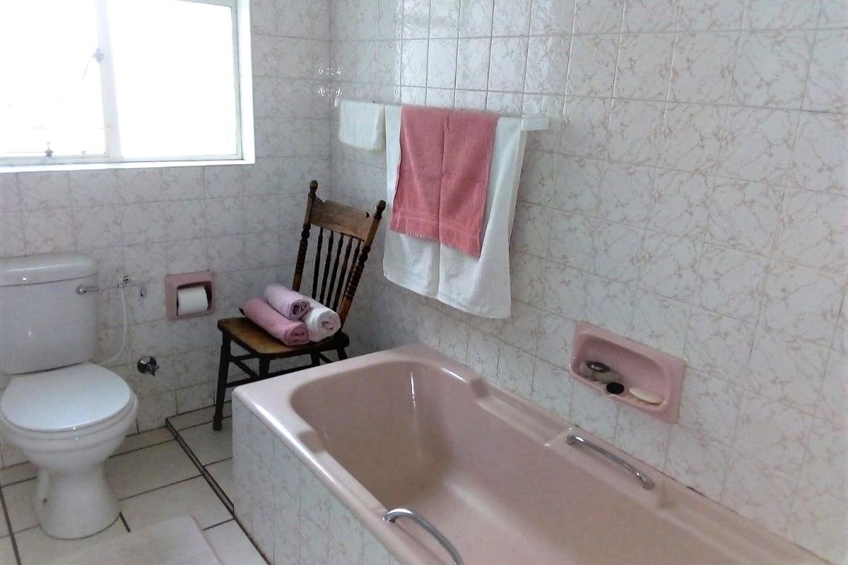 A dated bathroom featuring a pink built-in bathtub, white toilet, and patterned wall tiles with a recessed soap holder.