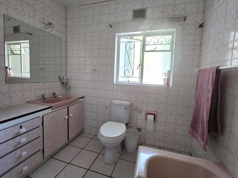 A dated bathroom featuring original pink sanitaryware, tiled walls and flooring, and a built-in vanity unit with storage.