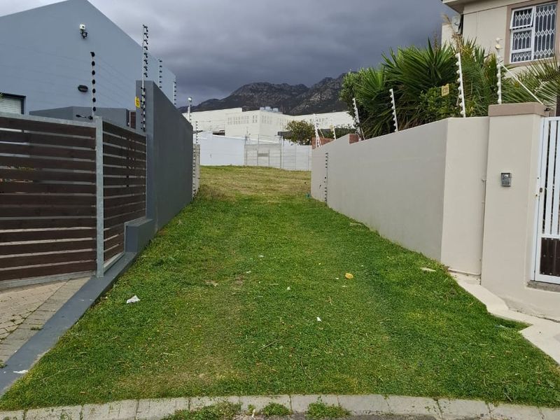 A vacant residential plot situated between two existing properties, featuring established boundary walls and electric fencing, ready for development.