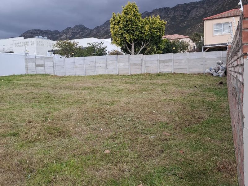 A vacant residential plot featuring a grassed surface, enclosed by precast concrete and brick boundary walls with installed electric fencing.