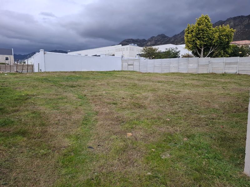 A vacant residential plot featuring a grassed surface and enclosed by precast concrete boundary walls, set against a mountain backdrop.