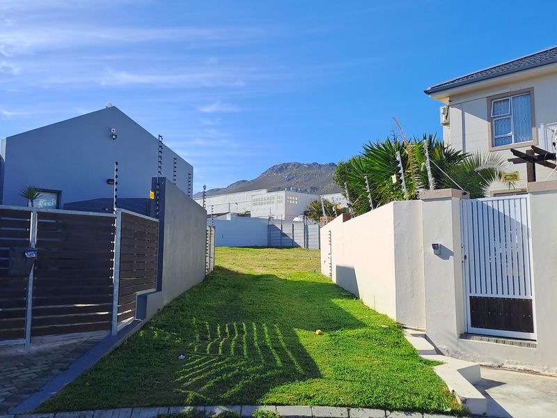 A vacant residential plot situated between two existing properties, featuring established boundary walls, electric fencing, and gated access from the street.