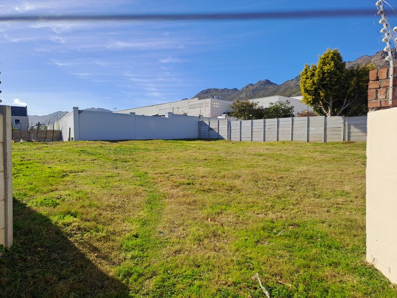 A vacant residential plot featuring a grass lawn, enclosed by perimeter walls with integrated electric fencing and mountain views in the background.