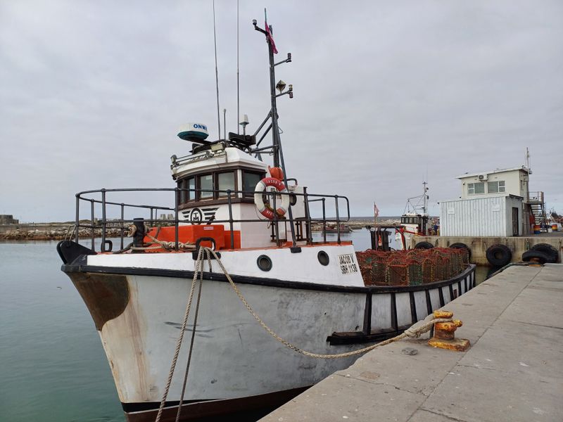 A fishing vessel docked at a concrete pier in a harbour setting.