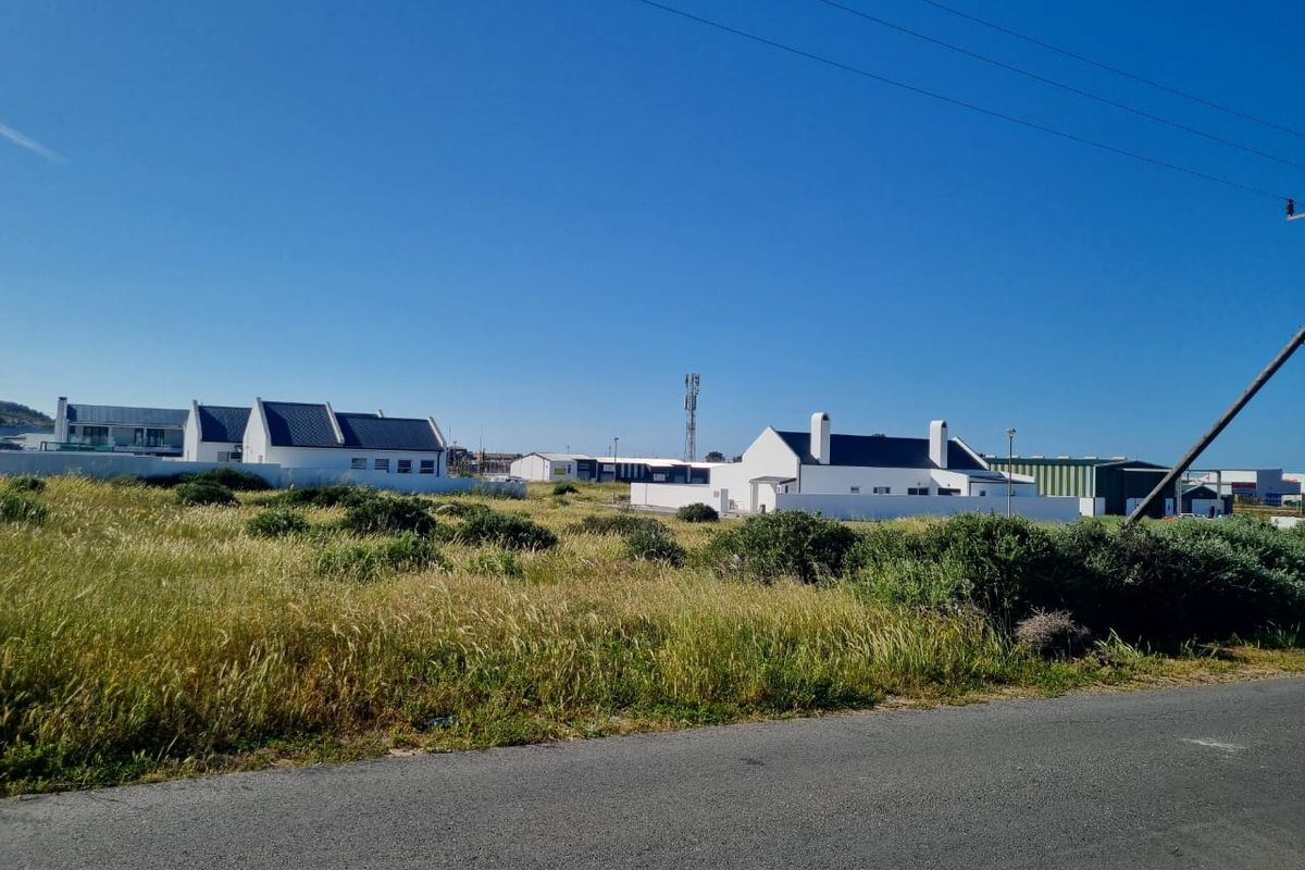 A vacant residential plot featuring natural vegetation, situated in a developed area with surrounding residential and commercial properties.