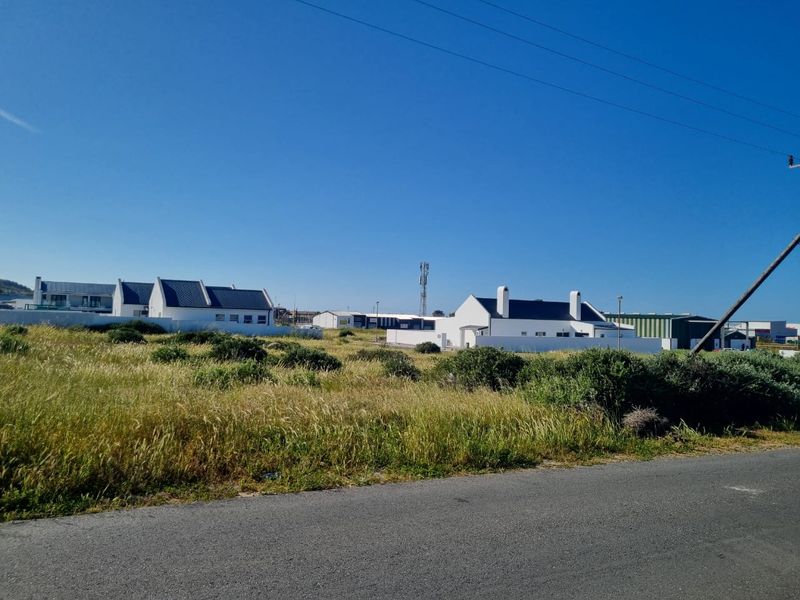 A vacant residential plot featuring natural vegetation, situated in a developed area with surrounding residential and commercial properties.