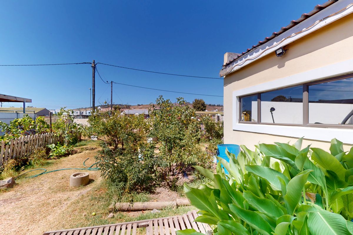 Rear garden area featuring a picket fence, established shrubs, and a view of the side elevation of the house with tiled roofing.