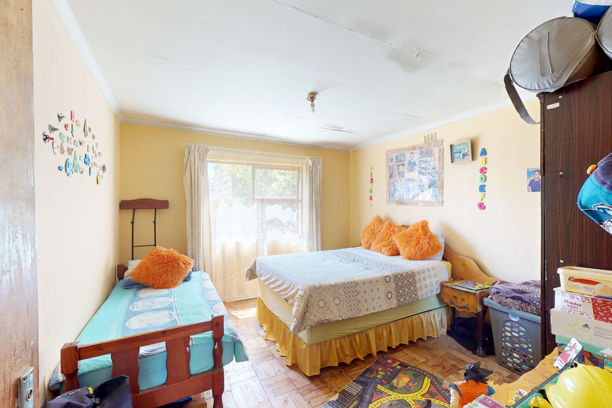 A bedroom featuring parquet flooring and a sliding window, currently showing signs of ceiling water damage and plaster cracking requiring maintenance.