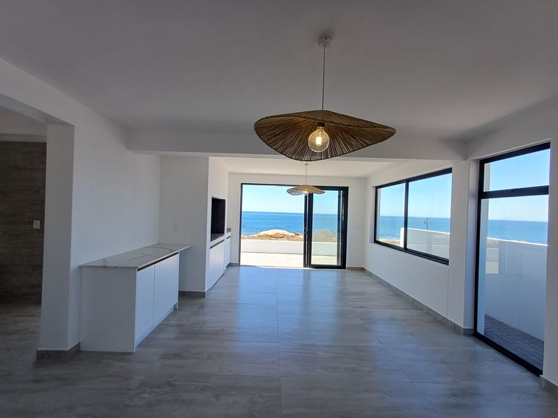 Spacious open-plan living area featuring large format floor tiles, built-in cabinetry, and expansive sliding glass doors offering panoramic ocean views.