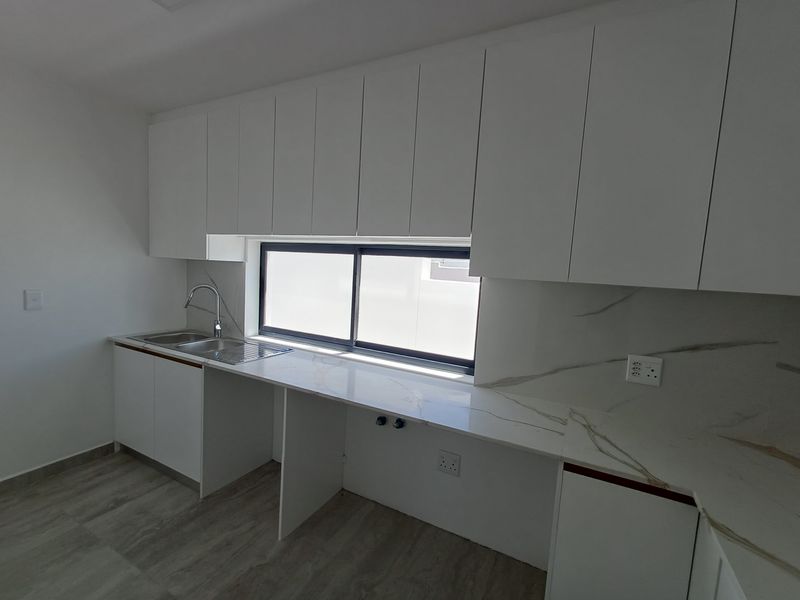Modern kitchen featuring white handleless cabinetry, marble-look stone countertops, a stainless steel sink, and a large sliding window for natural light.