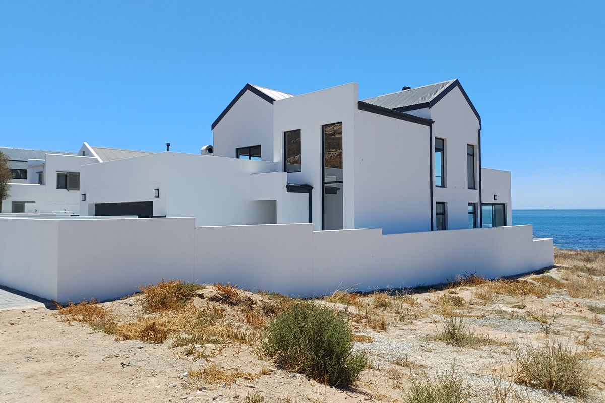 Modern coastal residence featuring a clean white facade, metal roofing, and large windows, situated in a prime location near the ocean.