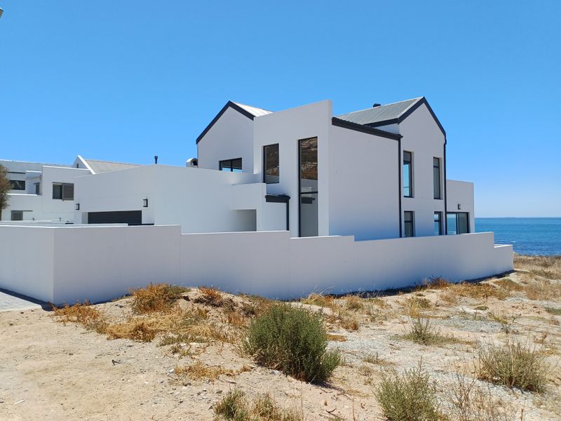 Modern coastal residence featuring a clean white facade, metal roofing, and large windows, situated in a prime location near the ocean.