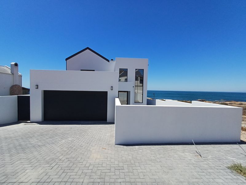 Modern coastal home featuring a clean white facade, paved driveway, and double garage with a scenic ocean view.