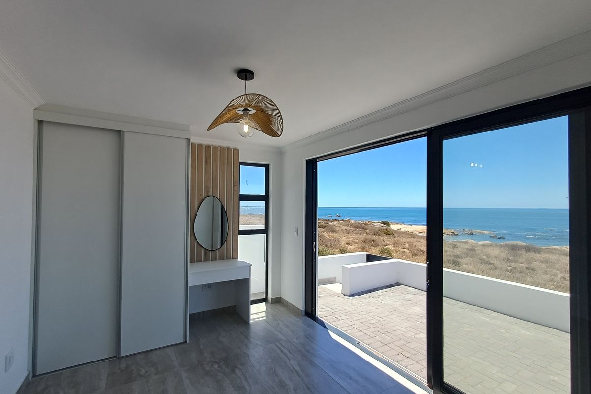 Modern bedroom featuring built-in cabinetry, a sleek vanity area, and large sliding doors opening onto a patio with stunning ocean views.