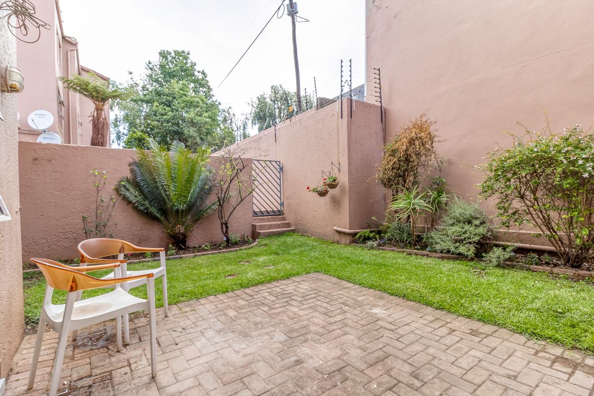 A private rear courtyard featuring a paved patio area, a small lawn, and perimeter boundary walls with security fencing.