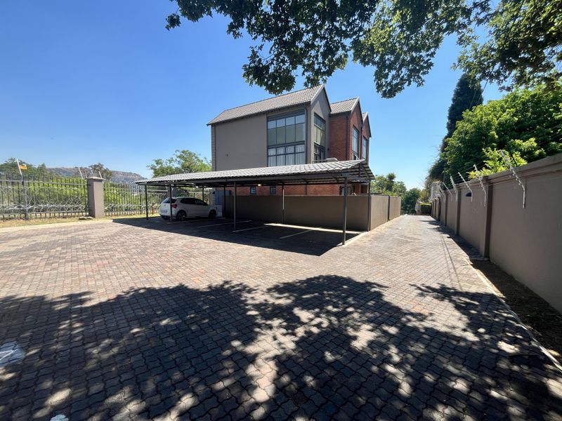 Exterior view of the apartment complex featuring a paved driveway, covered carport parking, and secure perimeter walling with electric fencing.