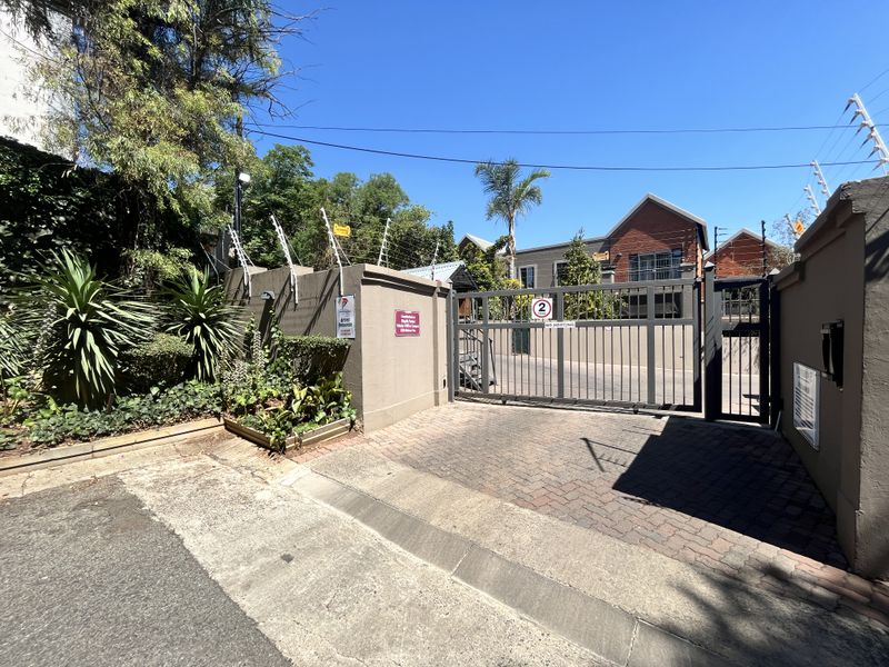 Secure gated entrance to the apartment complex featuring a paved driveway, perimeter walling with electric fencing, and a sliding security gate.