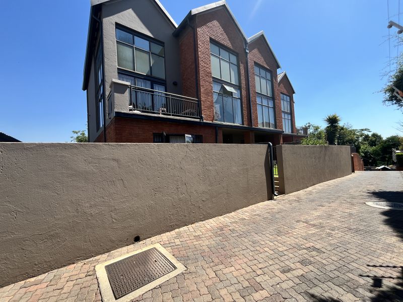 Front exterior view of a multi-story apartment building featuring brick and rendered facade, large windows, and a private balcony, accessed via a paved driveway.