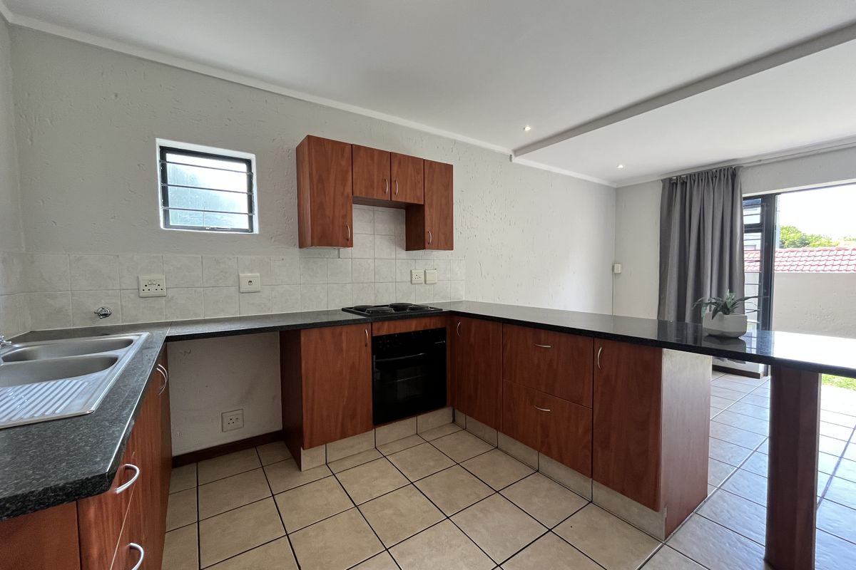 Functional kitchen featuring wood-finish cabinetry, dark countertops, built-in oven and hob, tiled flooring, and a breakfast bar overlooking the living area.
