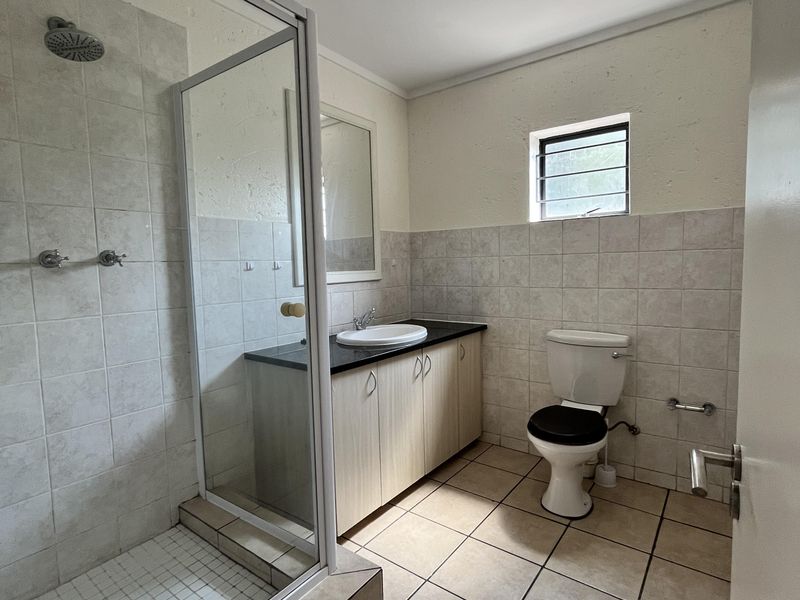 A functional bathroom featuring a glass-enclosed shower, vanity cabinet with basin, toilet, and neutral tiled finishes throughout.