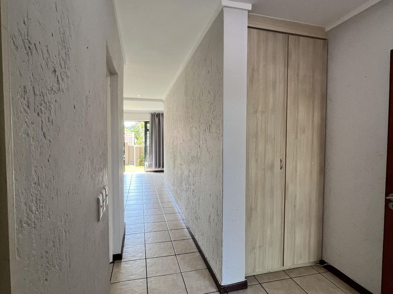A bright, tiled hallway featuring a built-in cupboard and textured wall finishes, leading towards an open living area.