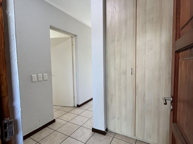 A clean, empty hallway featuring neutral tiled flooring and built-in wooden cupboards, providing functional storage space within the apartment.