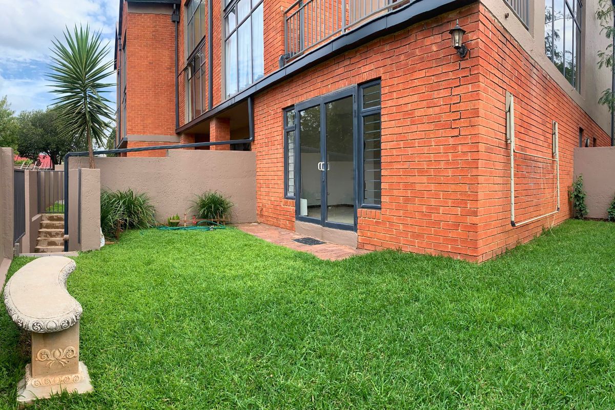 Rear view of the apartment featuring a private garden, brick facade, and direct access via glass sliding doors to the living area.