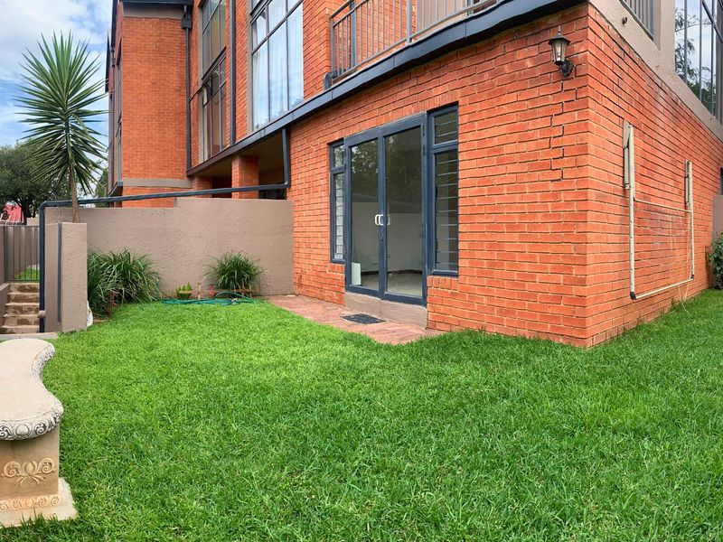 Rear view of the apartment featuring a private garden, brick facade, and direct access via glass sliding doors to the living area.