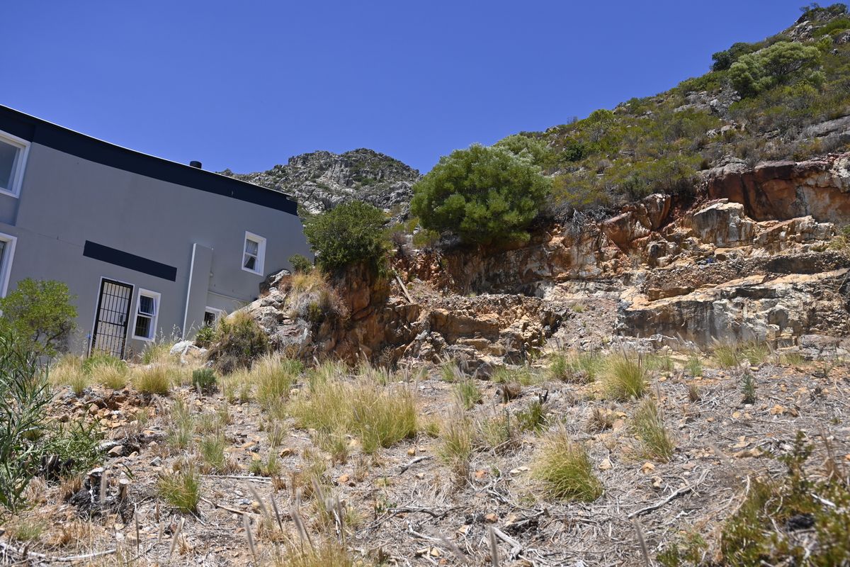 A view of the rear exterior of the property, showcasing the natural rocky terrain and slope adjacent to the building structure.
