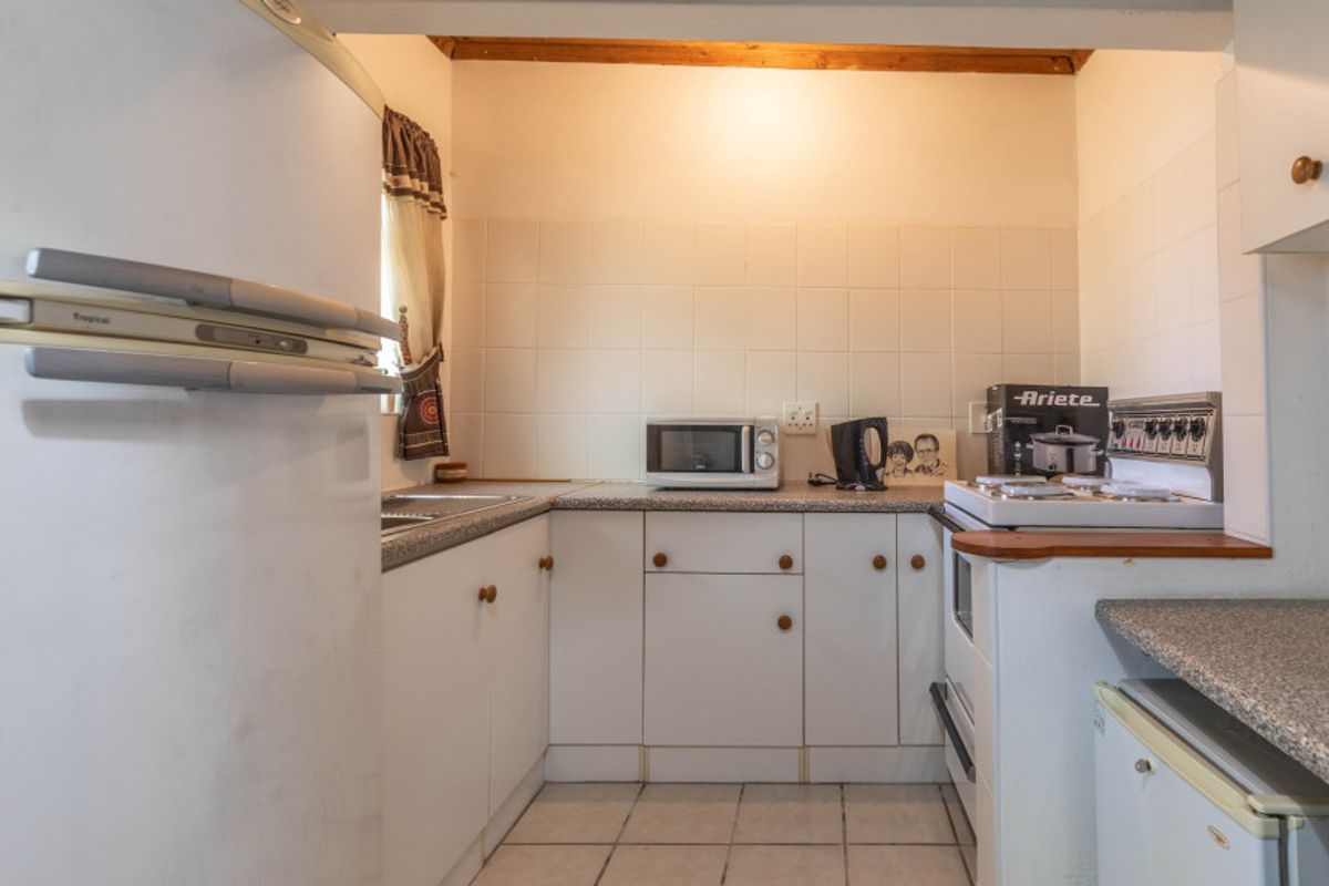 A compact, dated kitchen featuring white cabinetry, tiled splashbacks, and a functional layout with built-in stove and sink area.