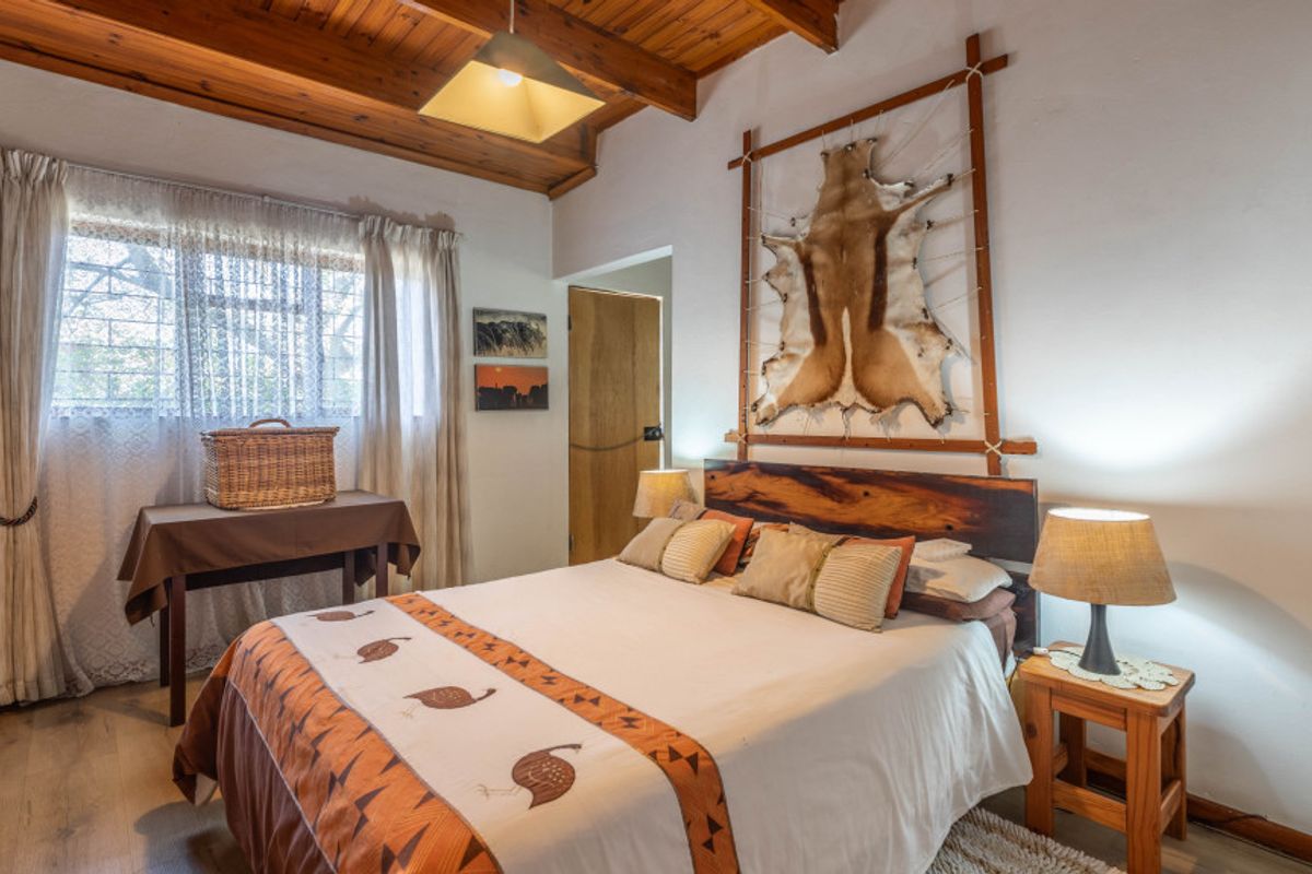 A cozy bedroom featuring exposed timber ceiling beams, laminate flooring, and a built-in wooden headboard.