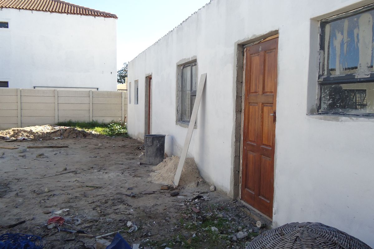 Exterior view of a property under construction, featuring unfinished wall plaster, exposed door frames, and an unlandscaped rear yard area.