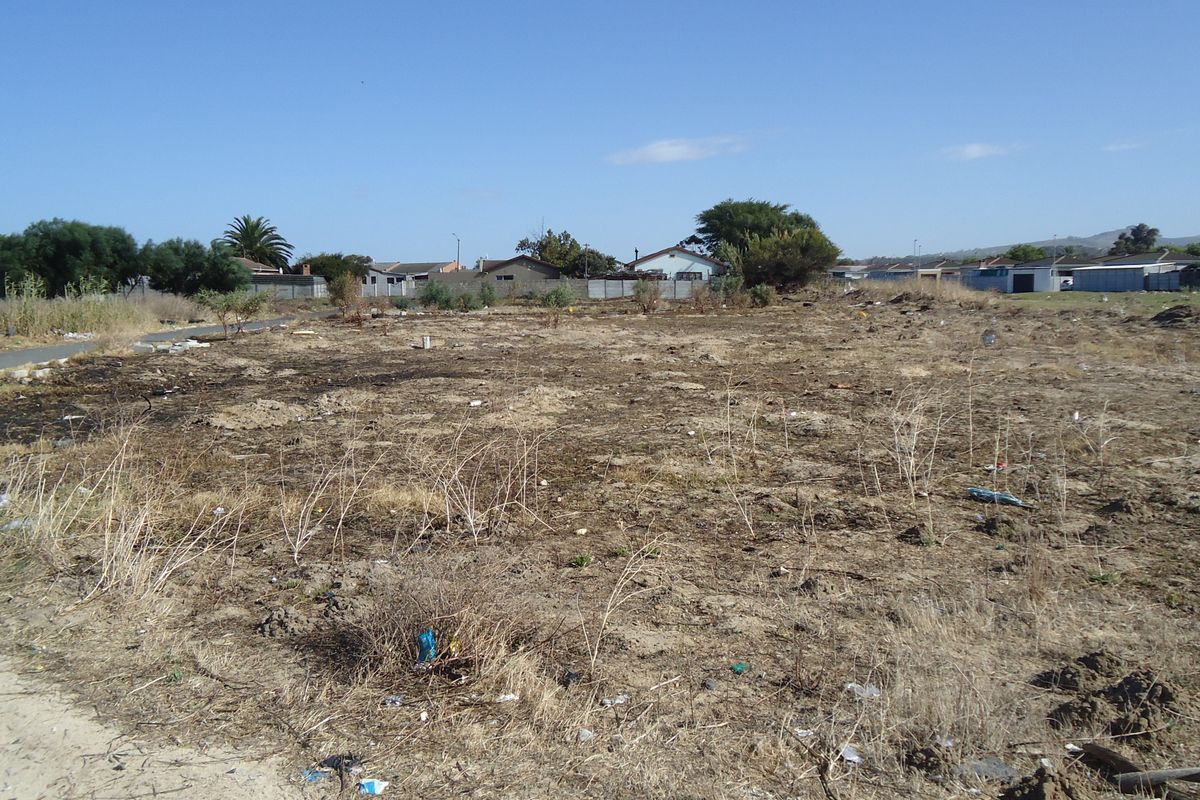 A vacant residential plot of land featuring dry, unimproved ground with surrounding neighborhood residential properties visible in the background.