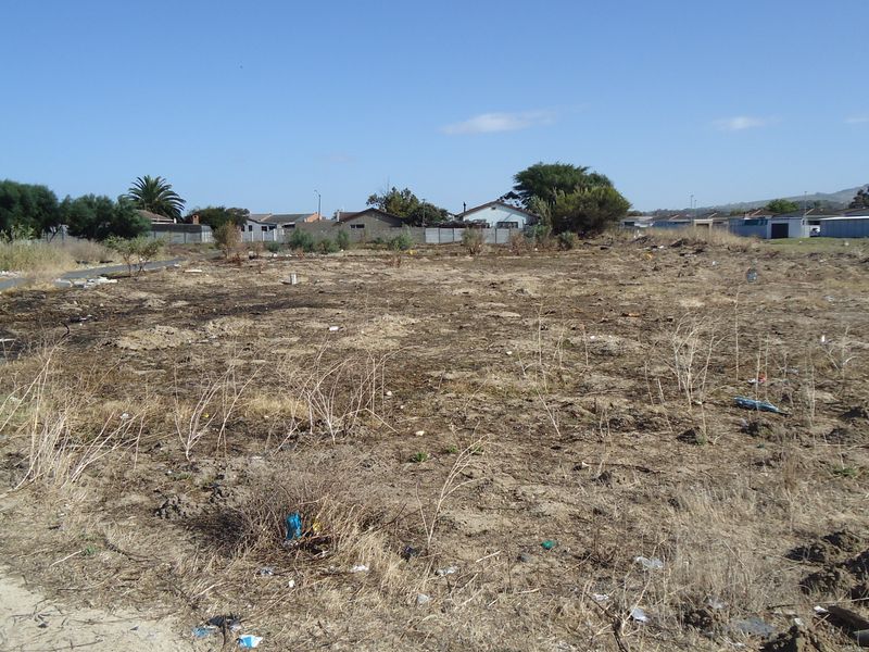A vacant residential plot of land featuring dry, unimproved ground with surrounding neighborhood residential properties visible in the background.