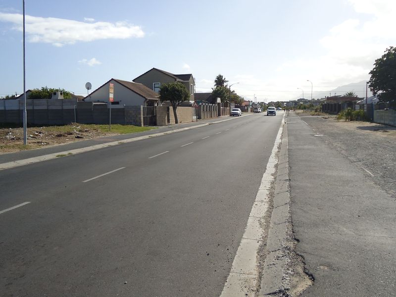 A view of the residential street frontage showing the asphalt road, concrete curbing, and surrounding boundary walls of the neighborhood.