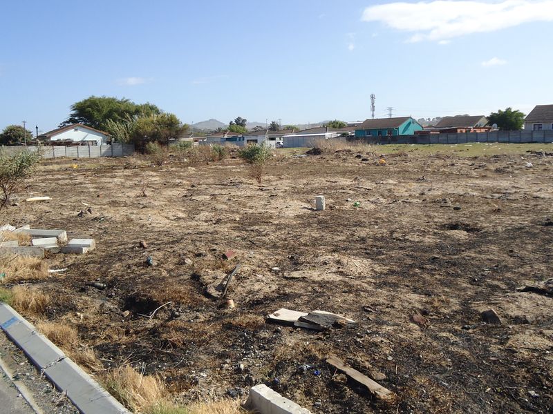 A vacant residential plot featuring a concrete curb and perimeter boundary wall, currently showing signs of scorched vegetation and debris.