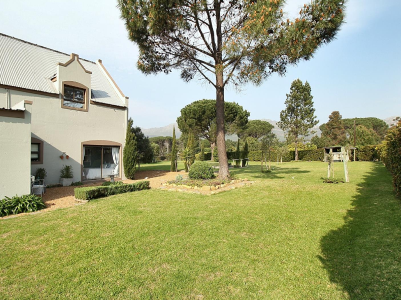 A spacious rear garden featuring a well-maintained lawn, mature trees, and a view of the property's rear elevation with a sliding door entrance.