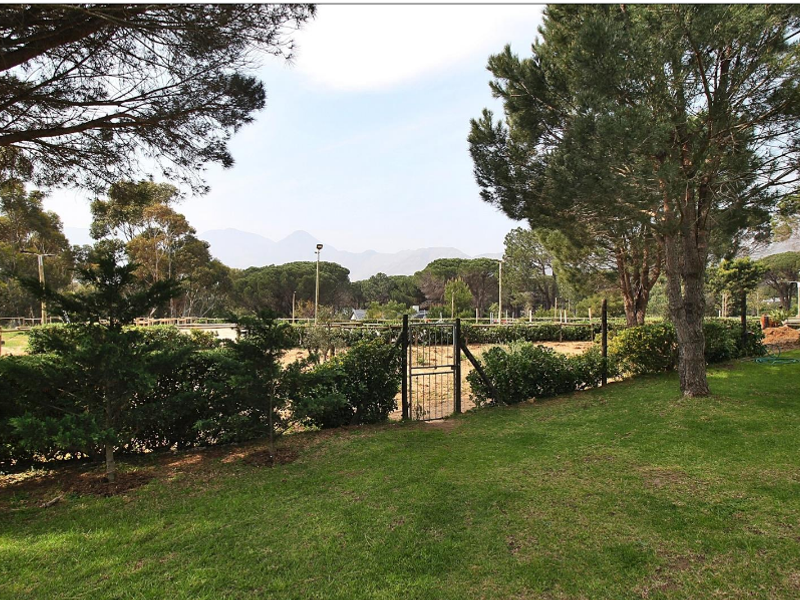 A well-maintained garden area featuring mature trees, a manicured lawn, and secure perimeter fencing with a metal gate, offering scenic mountain views.