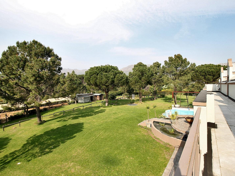 Spacious rear garden featuring a well-maintained lawn, mature trees, a swimming pool, and a paved walkway along the building exterior.