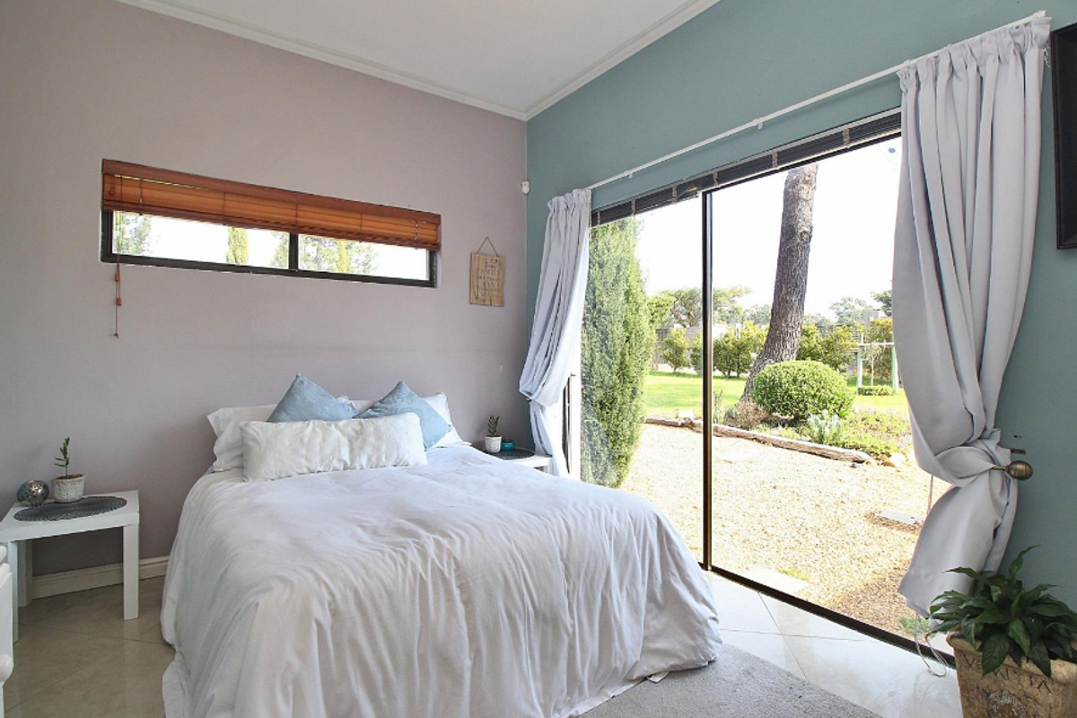 A bright bedroom featuring tiled flooring, a horizontal window, and a large sliding glass door providing direct access to the garden.